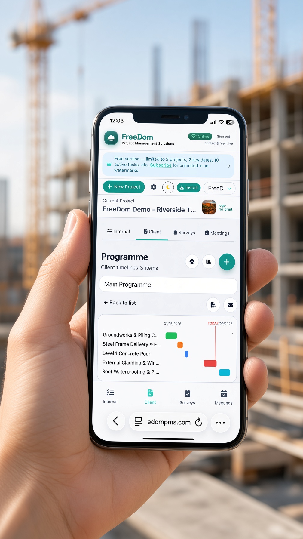 Hand holding phone on a construction site showing FreeDom client programme